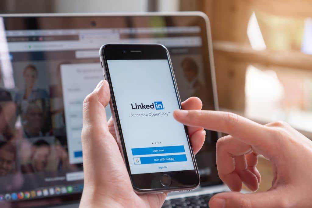 A business owner logs into his LinkedIn Business page from his phone, while LinkedIn is also pulled up on his laptop.