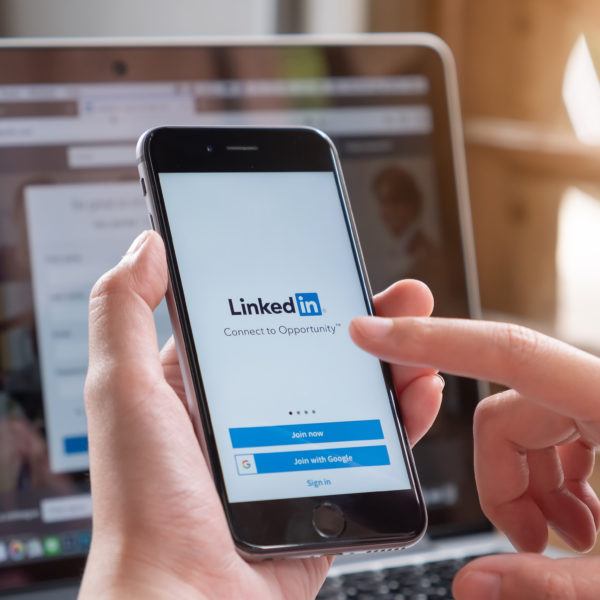 A business owner logs into his LinkedIn Business page from his phone, while LinkedIn is also pulled up on his laptop.