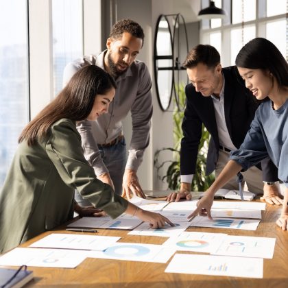Multiethnic Team Of Analysts Working On Paper Sales Reports, Analyzing Marketing Research Results, Discussing Strategy Of Growth, Development, Effective Business Plan, Investment